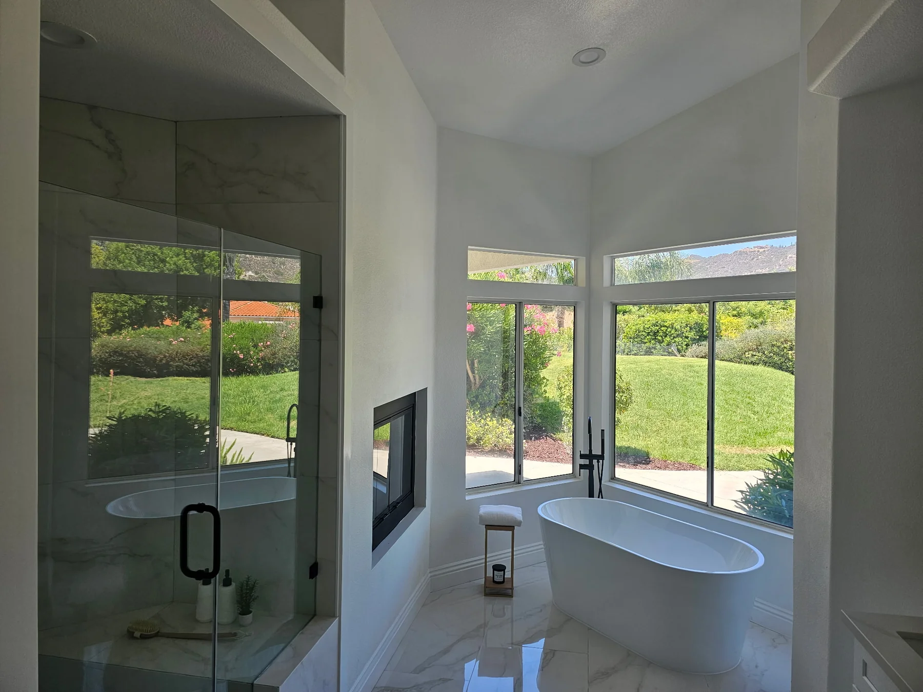 Glass shower and freestanding tub arranged beside corner windows in a remodeled bathroom.