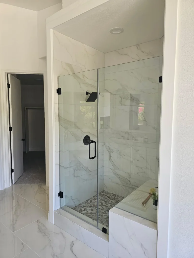 Glass shower enclosure with a tiled bench, veined tile walls and dark shower fixtures.