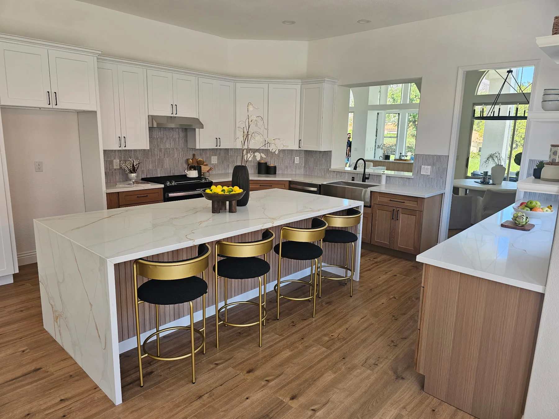 White upper cabinets, wood lower cabinets and a large island with four stools in a remodeled kitchen.